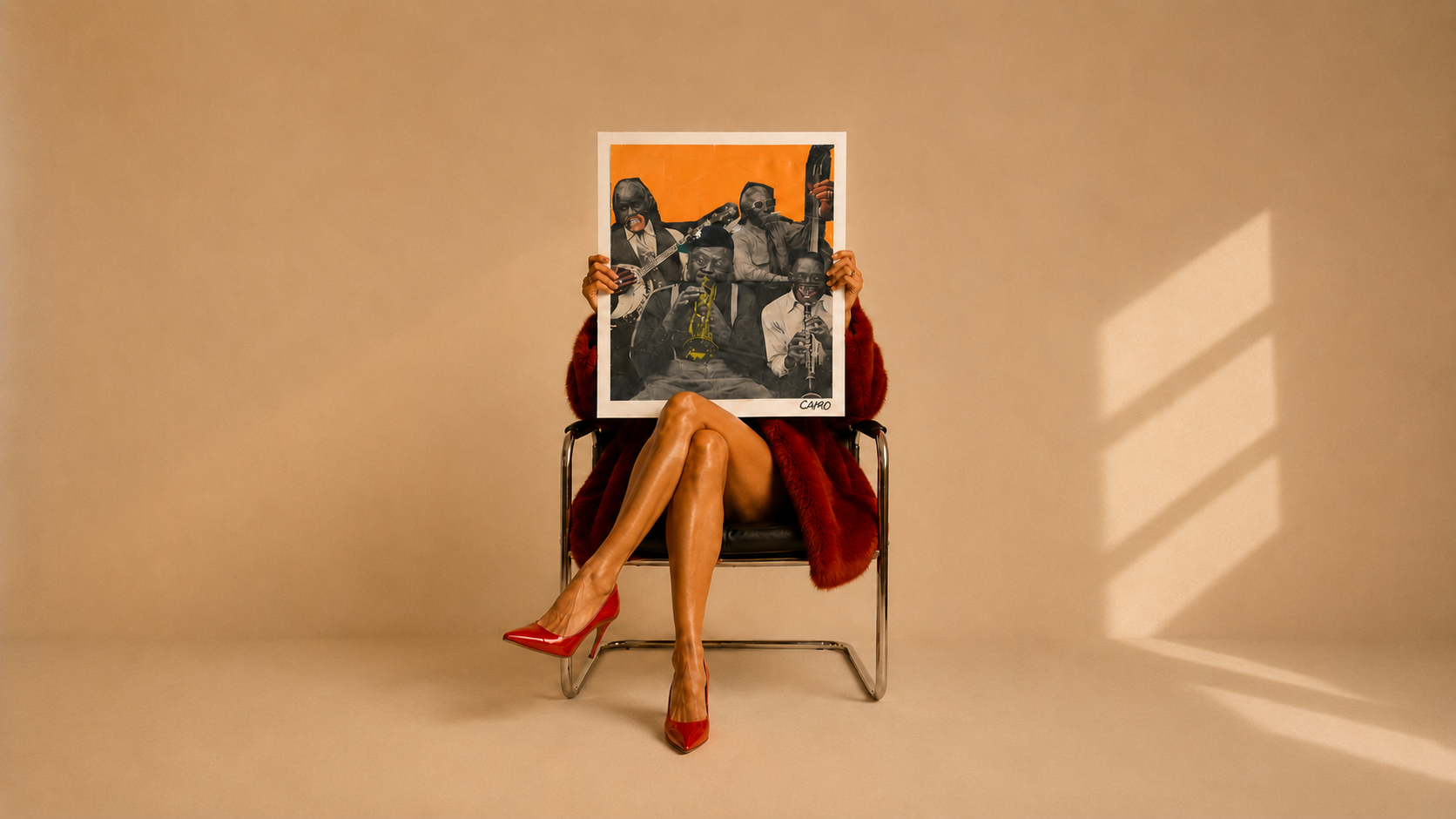 A person seated in a chair holds a framed art print in front of their face. The print features a black-and-white portrait of a group of musicians against a warm orange background.